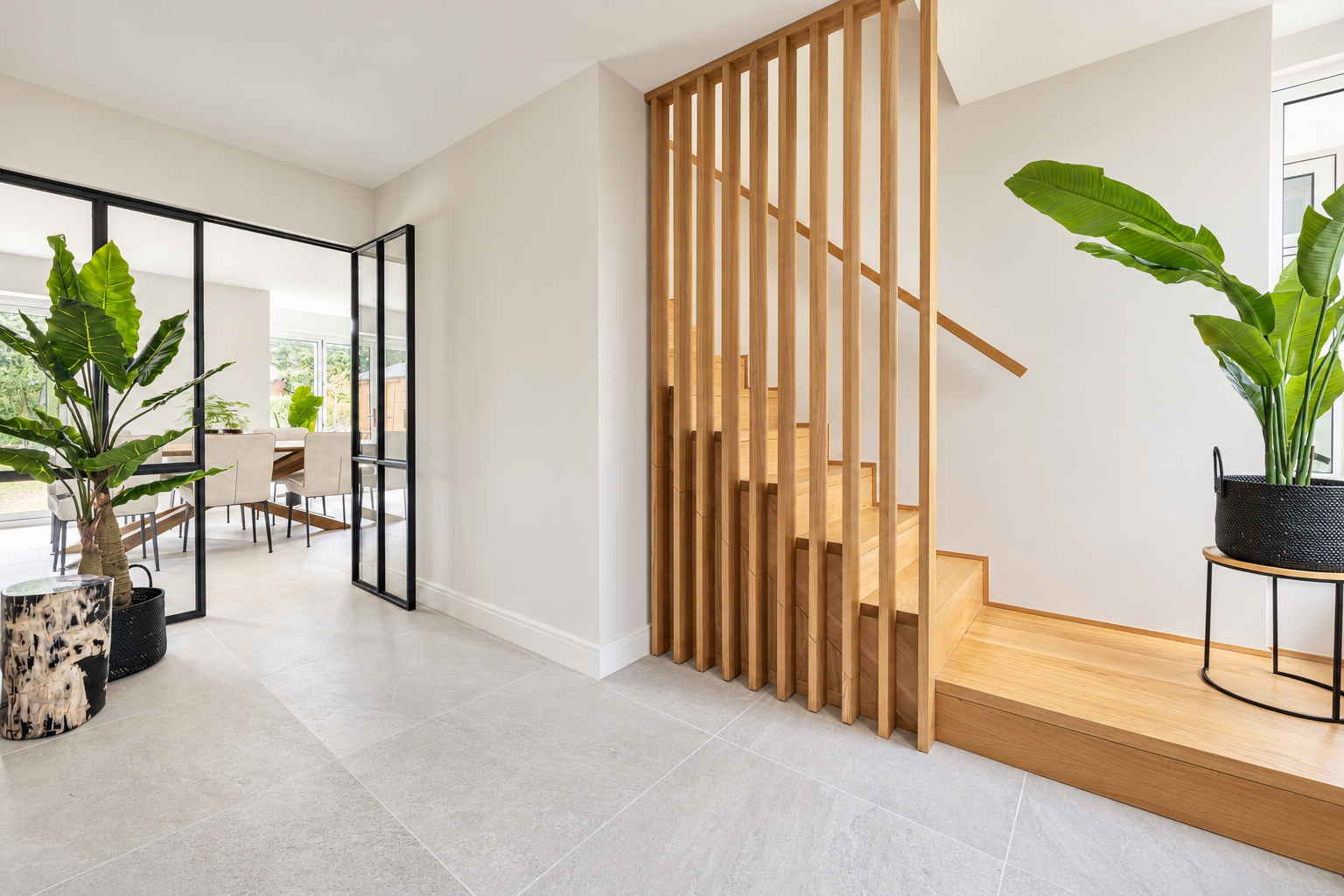 Oak staircase with vertical timber balustrade and black-framed glazed doors in the entrance hall at The Willows, Prestbury.