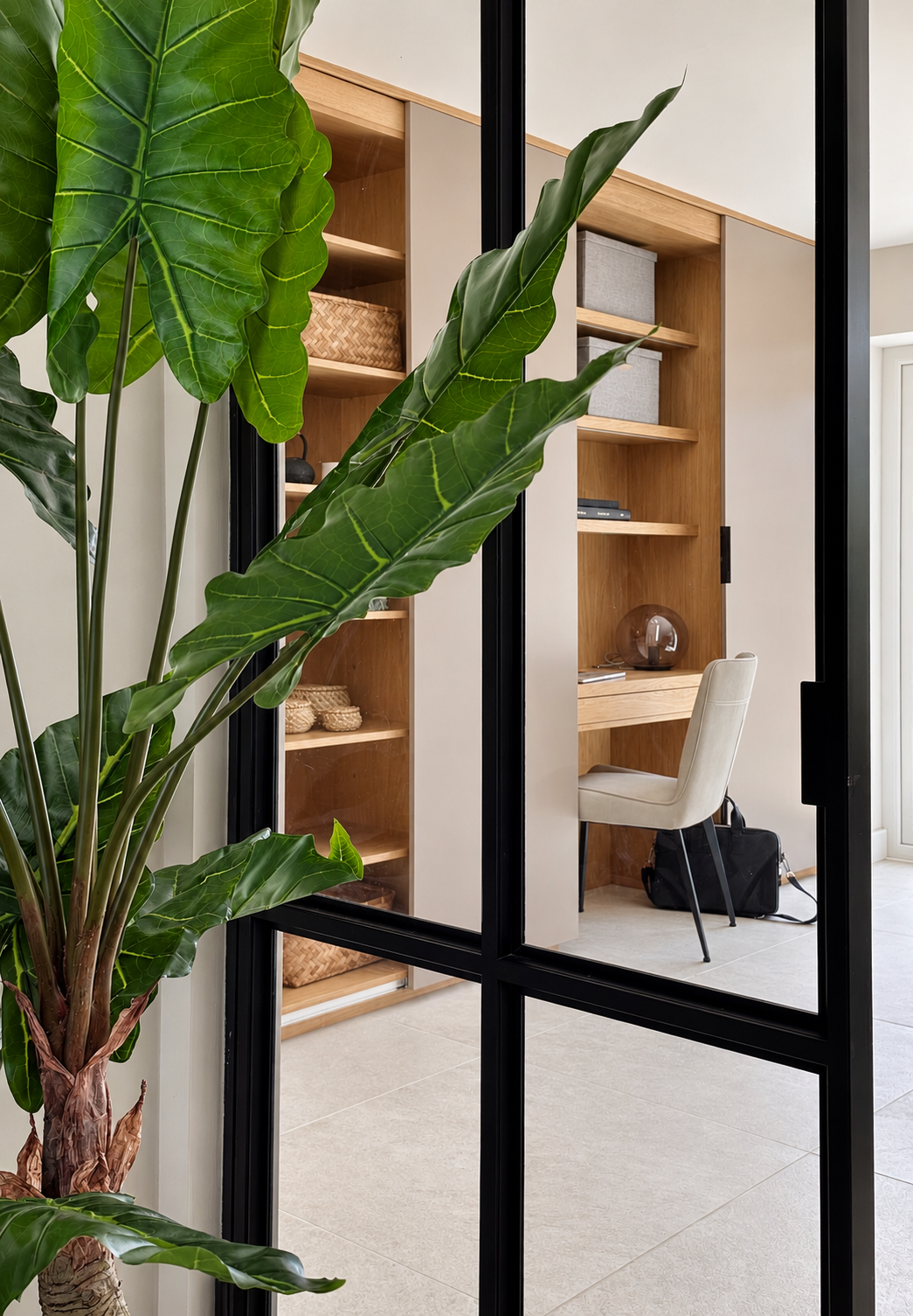 Oak desk and shelving seen through black-framed glazing beside a large leafy plant at The Willows, Prestbury.