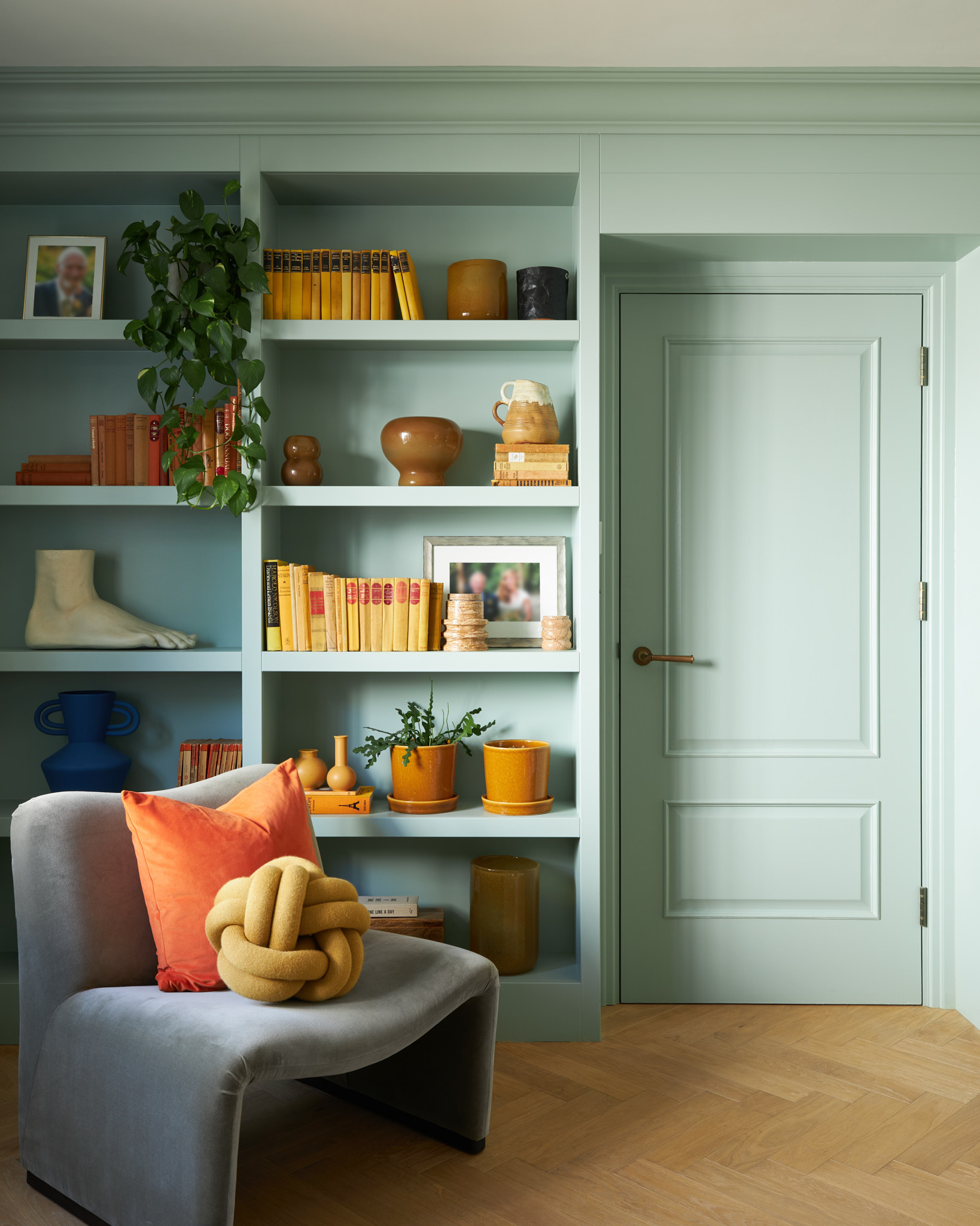 blue green bookcase with yellow and orange accessories.  Grey blue velvet occasional chair