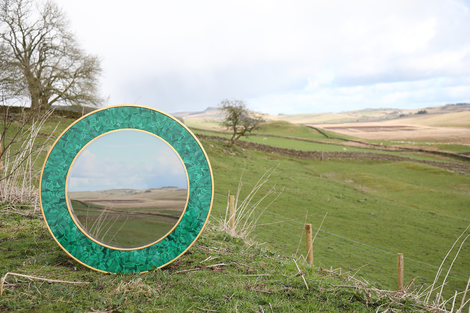 Circular mirror with green frame placed in the Northumberland landscape
