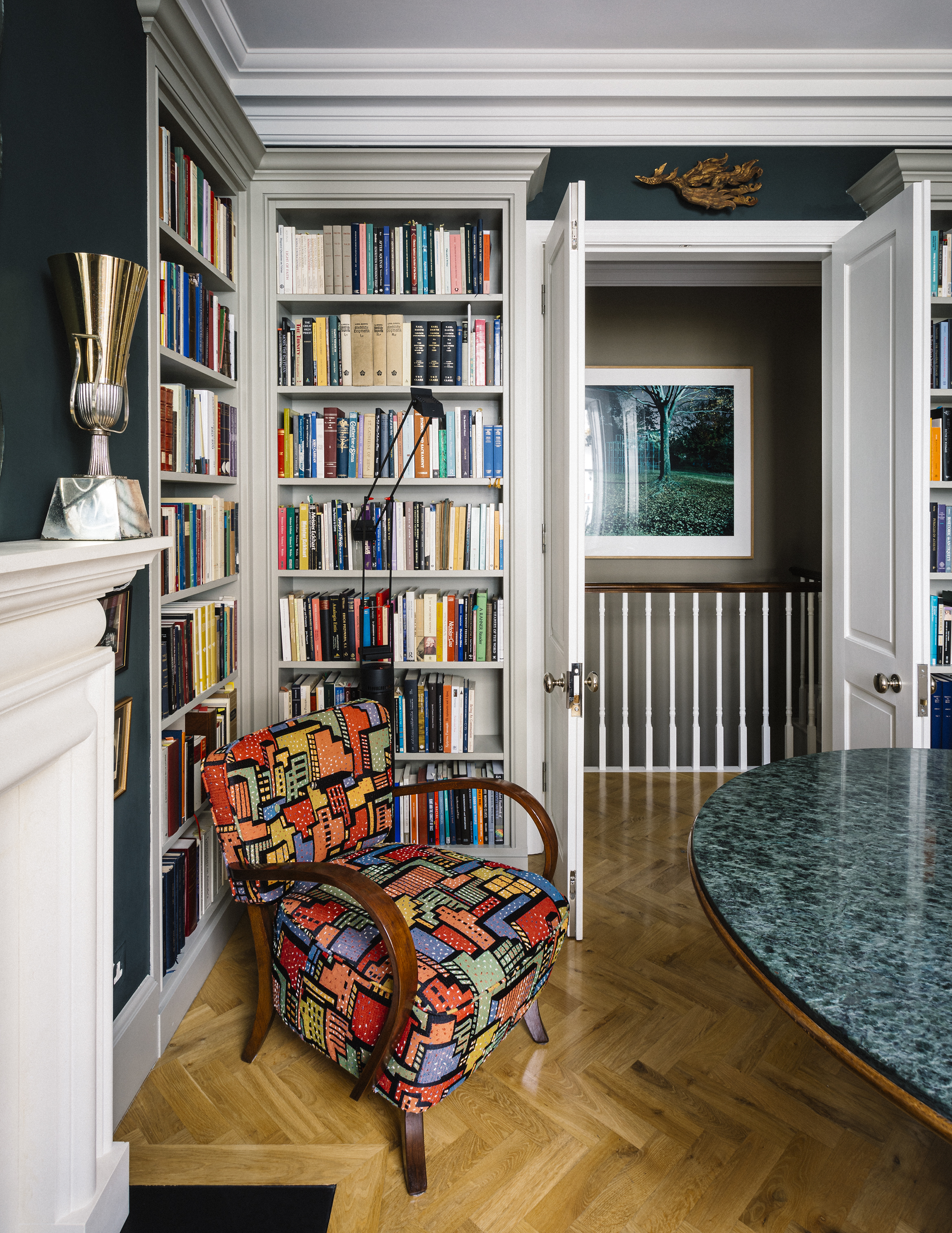 A pair of mid-century modern armchairs are surrounded by bespoke library joinery and earthy green shades