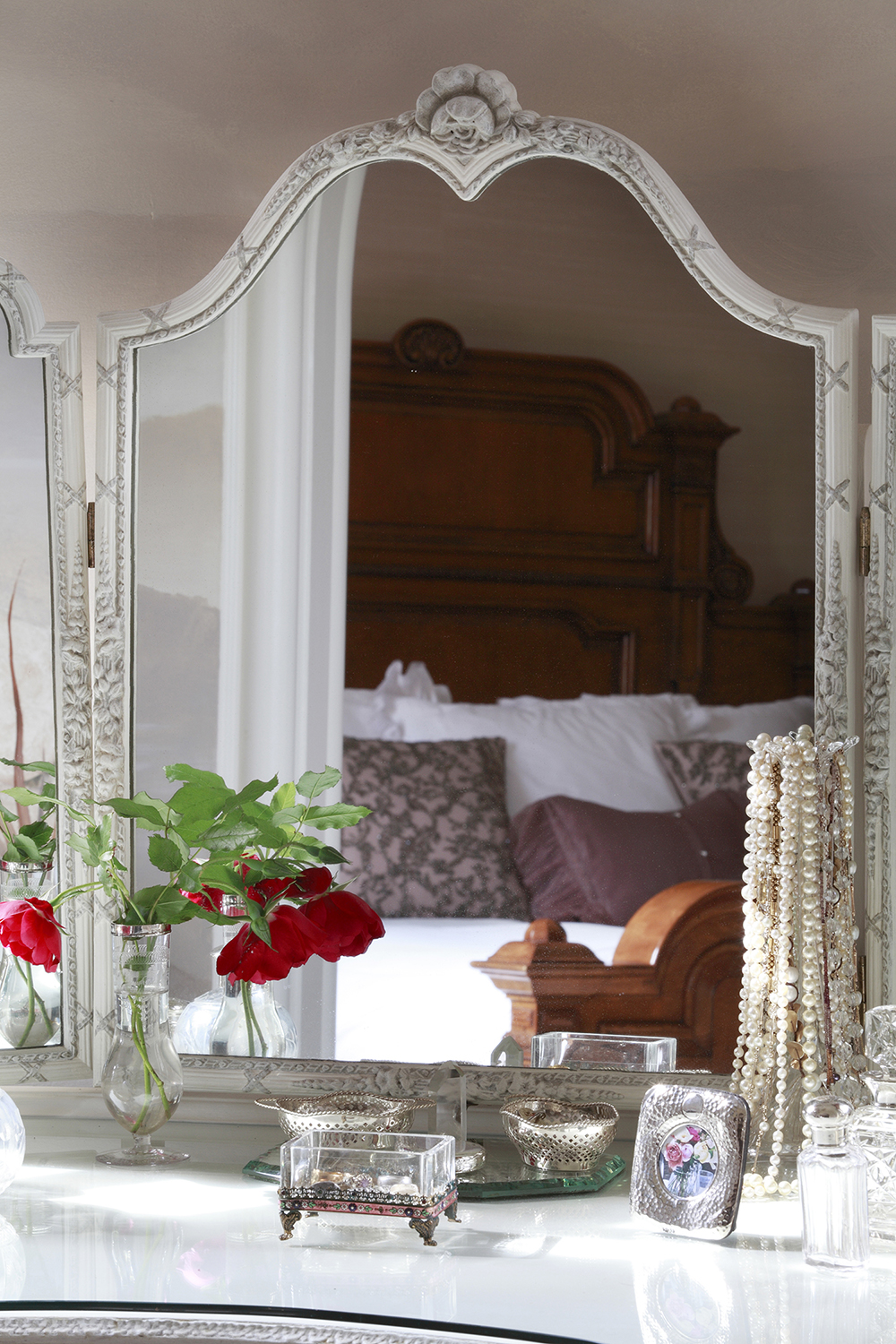 The high wooden Edwardian bedhead is reflected in the dressing table mirror.  