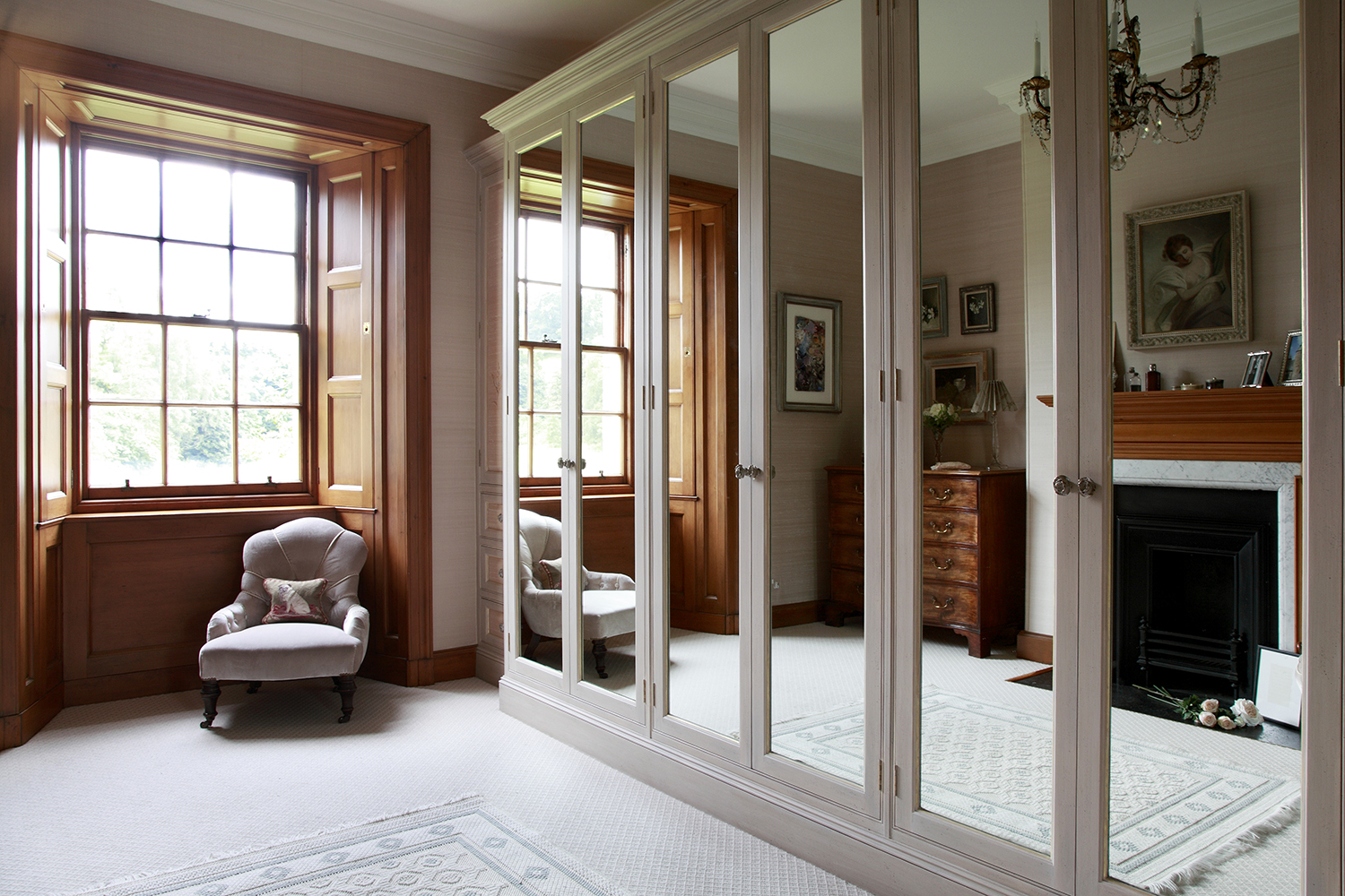 Tall mirror glass door fronts to the bespoke wardrobes have a gilt leaf inset detail and distressed brass rose handles.