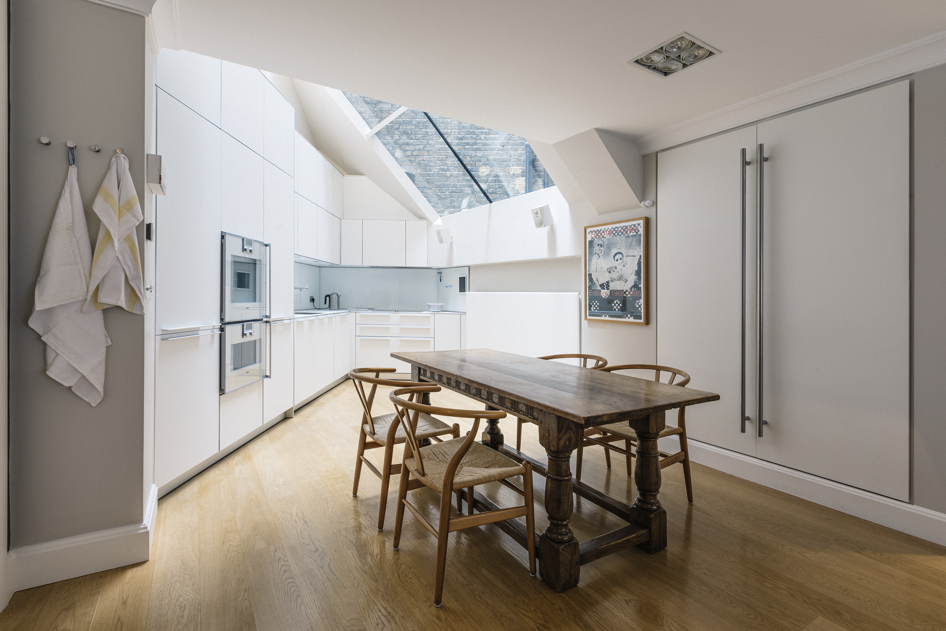 Opening up the roof allows light to poor into the basement kitchen. Strict and clean kitchen units are anchored by the classic rectory table and Mid-Century Modern chairs