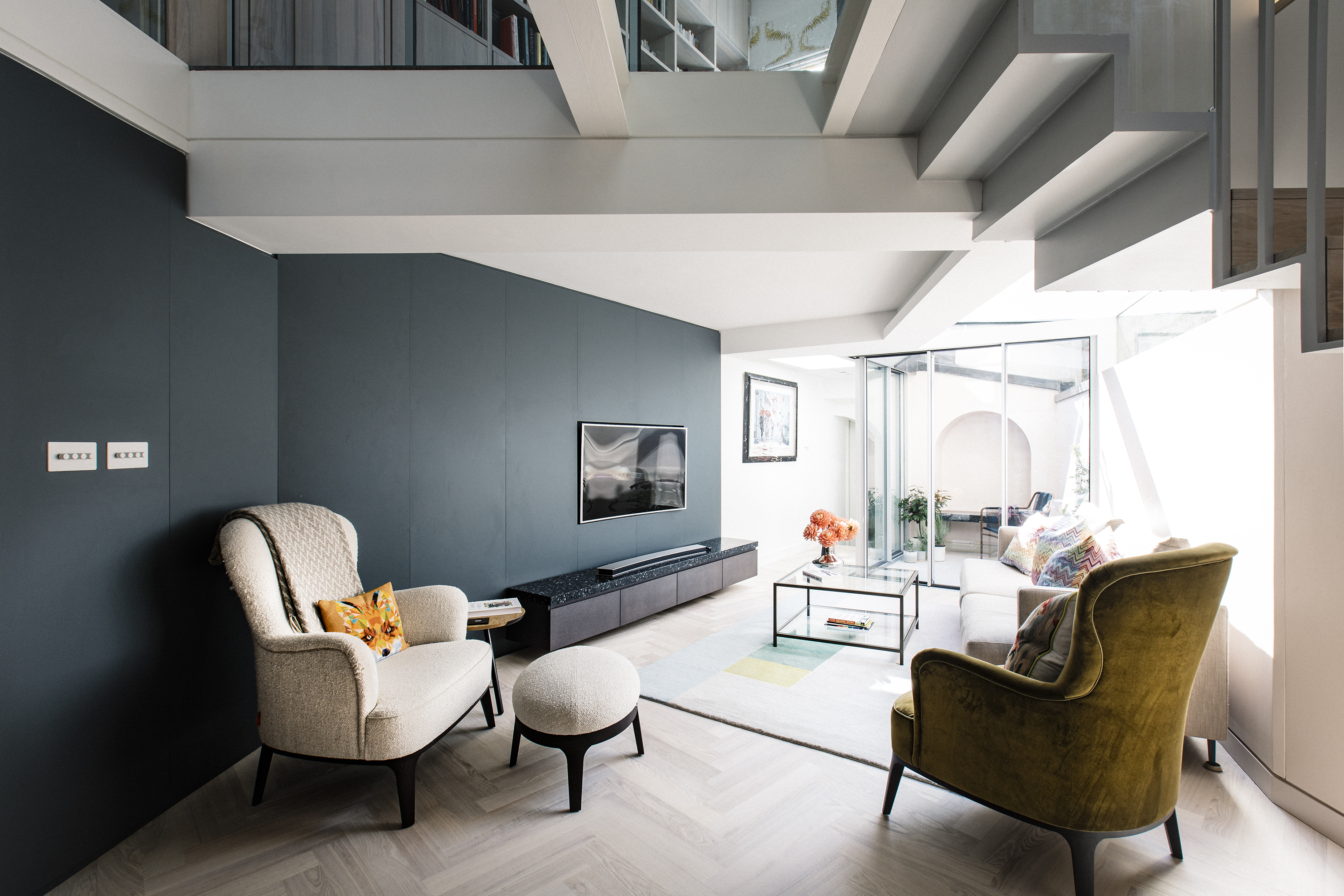 The curving petrol blue wall leads past modern armchairs from the TV room to the walled garden