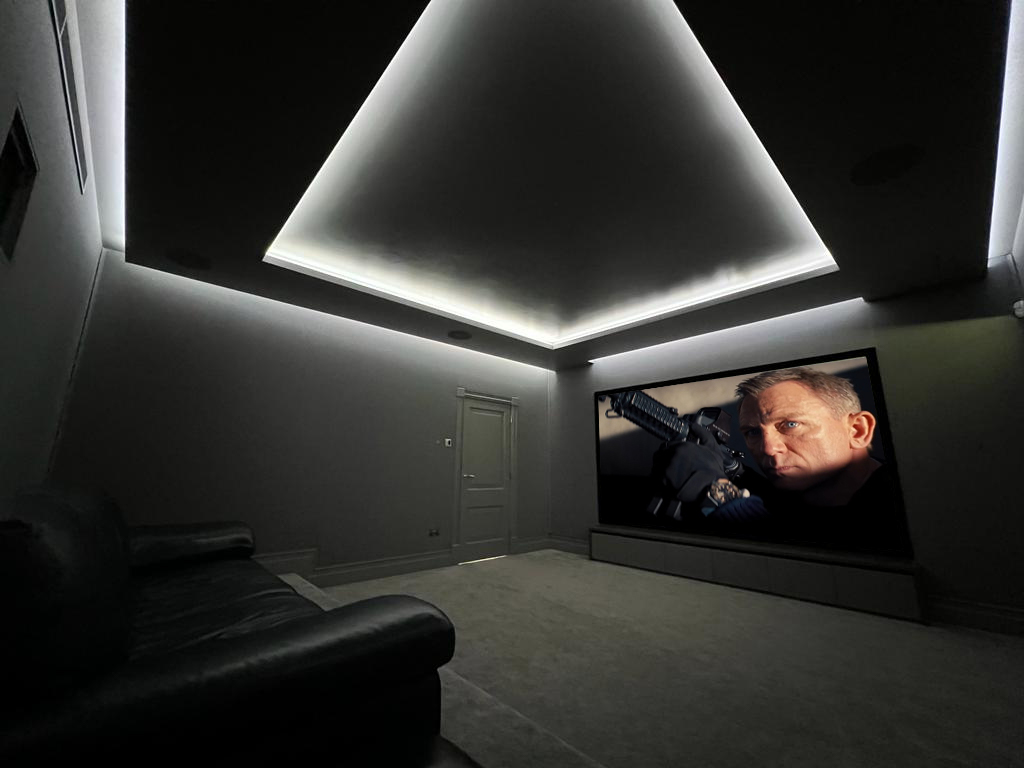 Small home cinema room with projector, screen and seating.