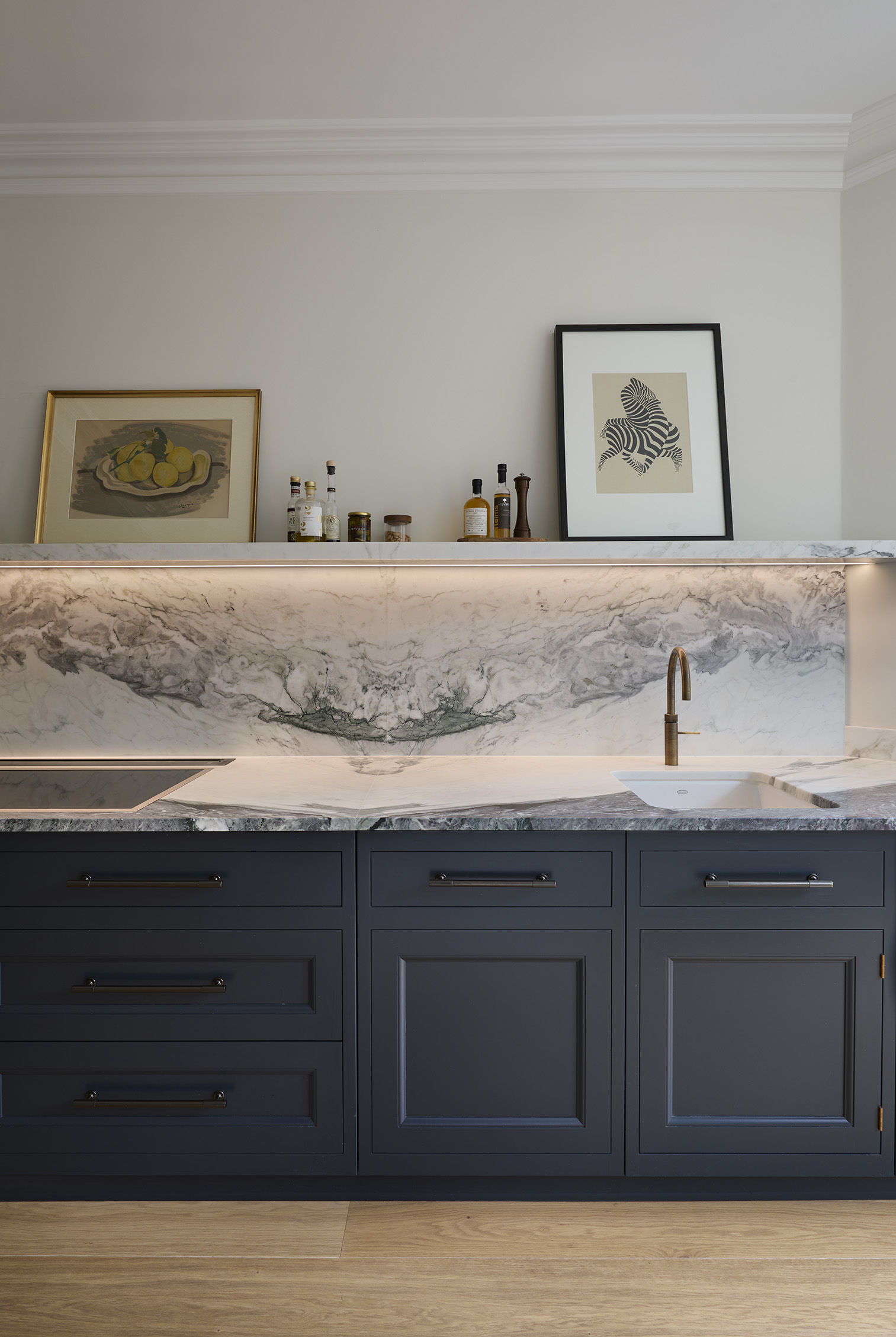 A detail view of a veined marble backsplash with shelf above dark grey base cabinets