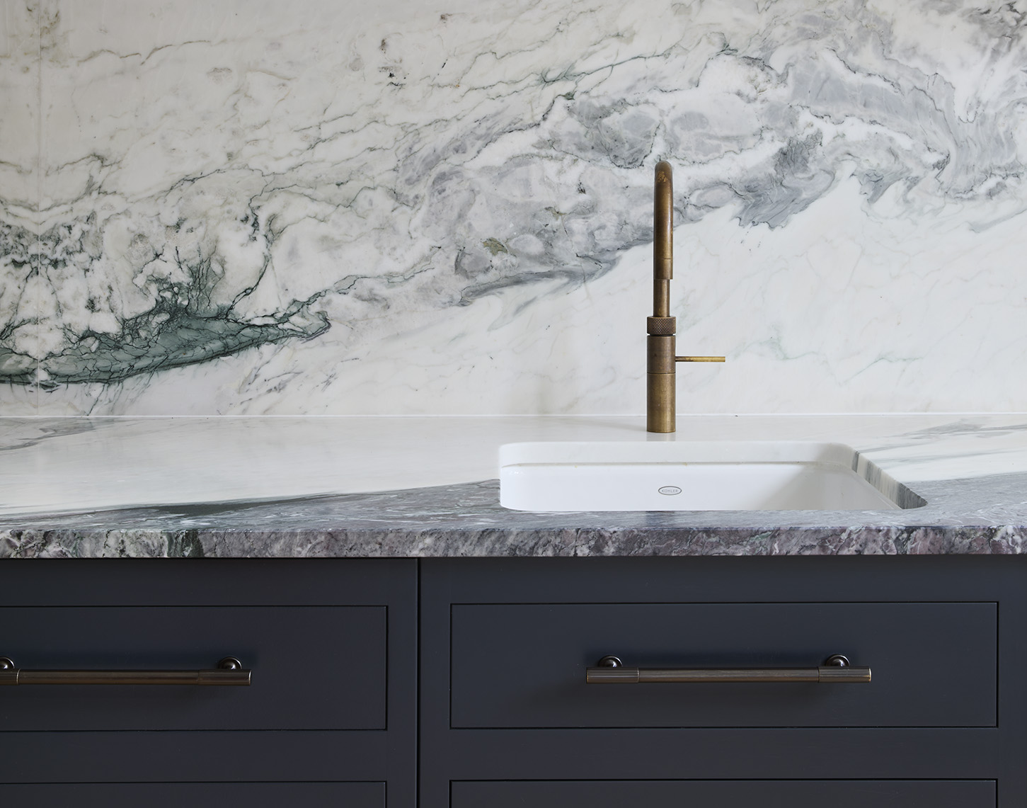 A detail shot of a hot water tap with marble backsplash and dark grey cabinets below.