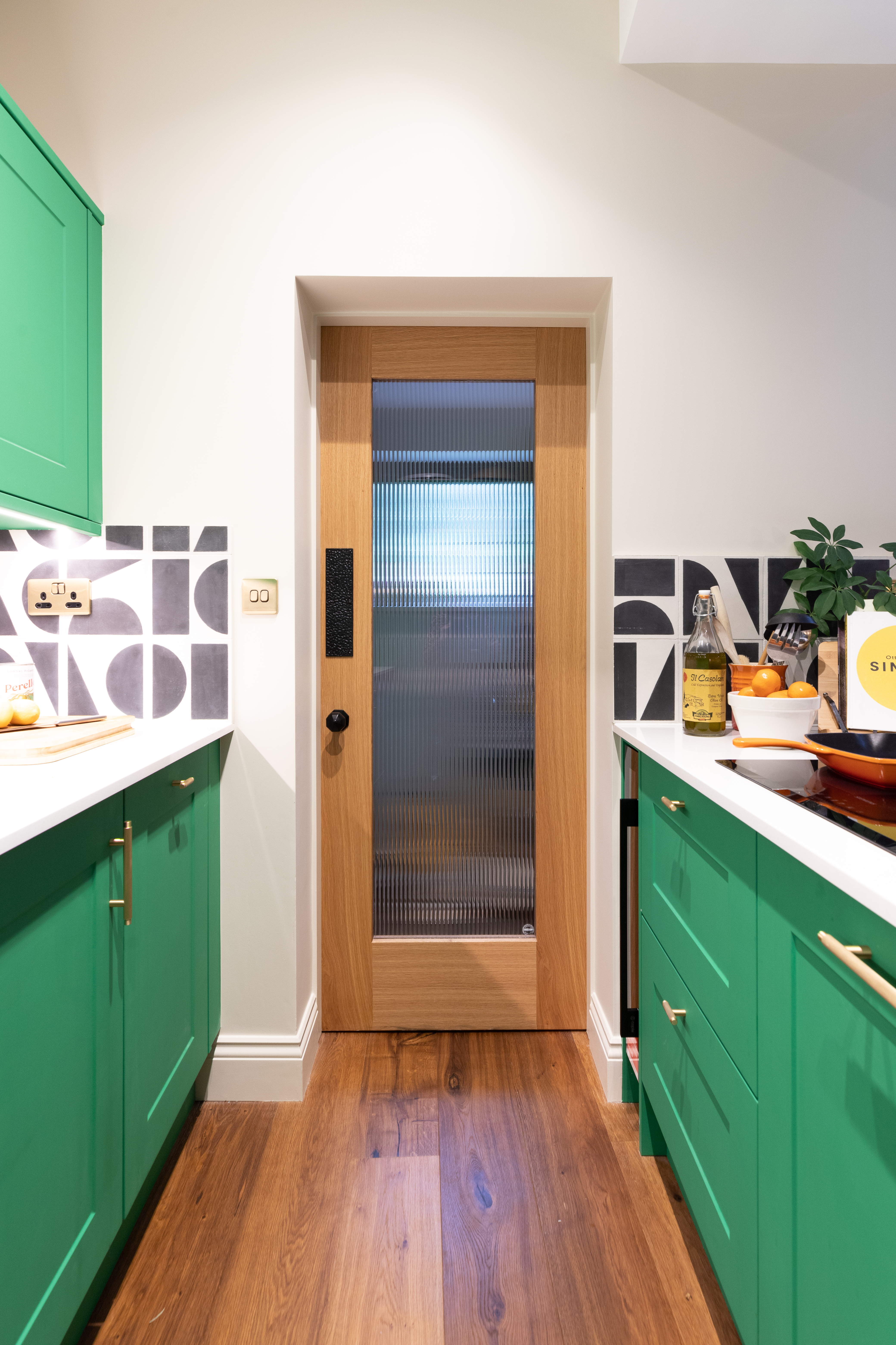 A gorgeous reeded glass door in the kitchen, looking exquisite with the bold green theme, brass ironmongery and feature tile splashback