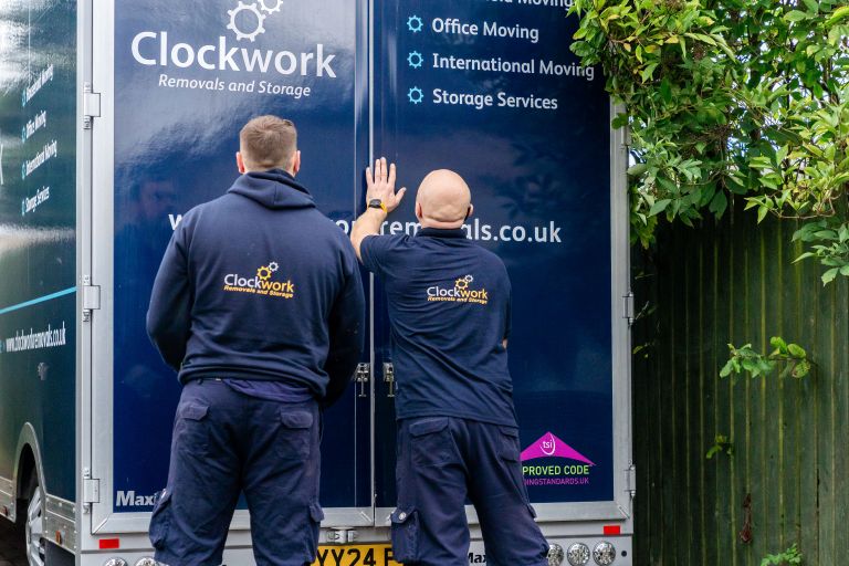 2 Clockwork Removal team members wearing branded clothes closing the back doors of a Clockwork Removals truck.
