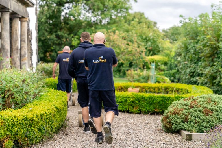 3 Clockwork Removals team members walking on a gravel path to an older building.