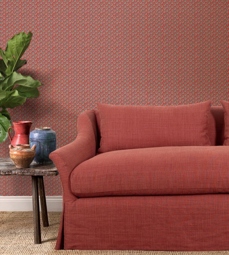 Red sofa with green plant to the left on a table with hugs and red and green patterned wallpaper behind