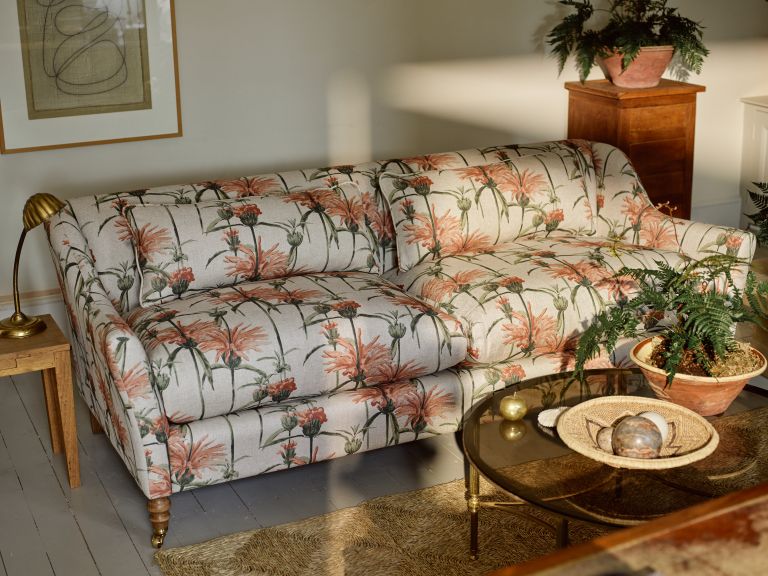 Two seater sofa with pink plants on with a coffee table and plant in front.