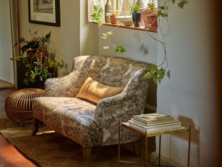 Small sofa under a window with plants hanging down and small table next to it.