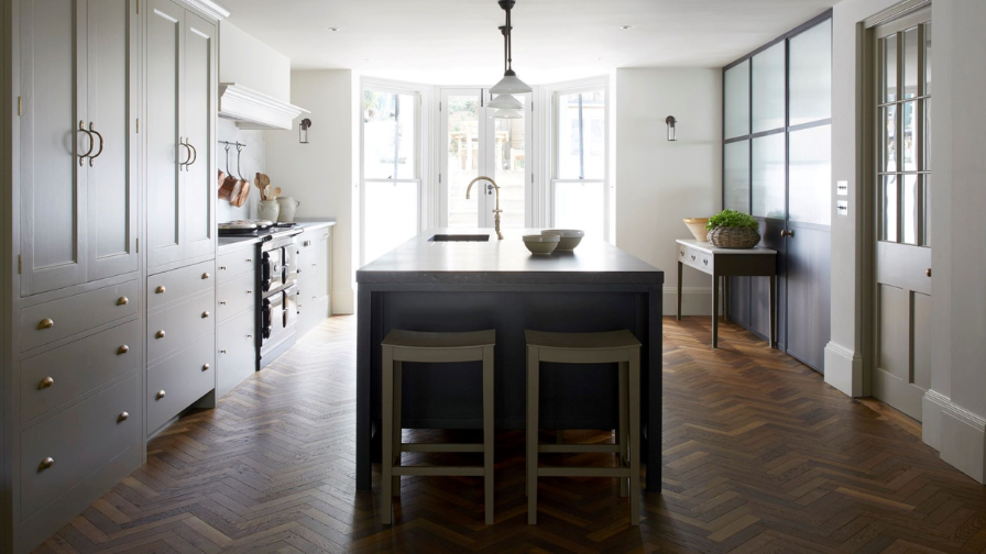 Kitchen with herringbone parquet and central island facing a bay window.