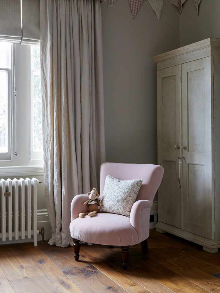 Interior of a bedroom featuring an oak floor, linnen curtains and a soft pink reading chair.