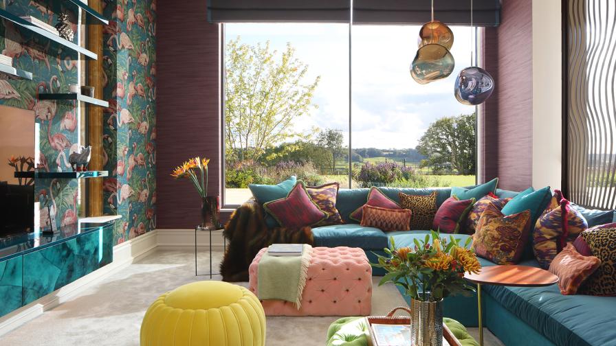 Colourful living room with huge windows framing views across the Cotswolds. Flamingo wallpaper and a teal coloured corner sofa with numerous cushions and button backed ottomans.