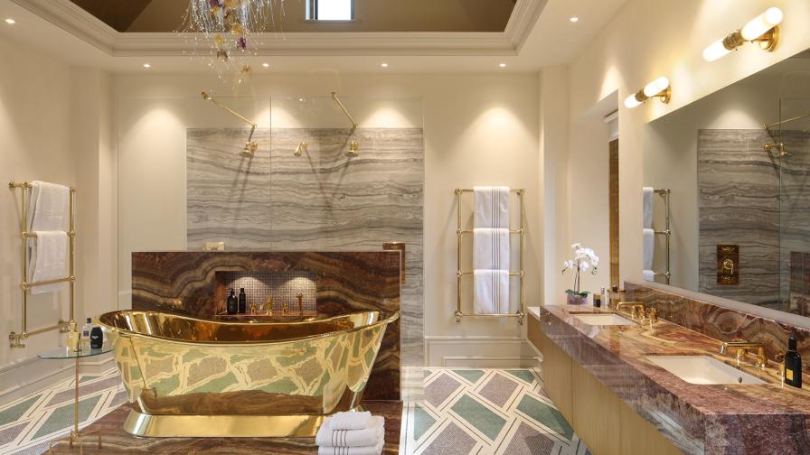 A gold bath on a marble podium is the focal point of the mosaic floored ensuite bathroom, which also includes twin basins in a marble vanity unit and a shower cubicle with three shower heads.