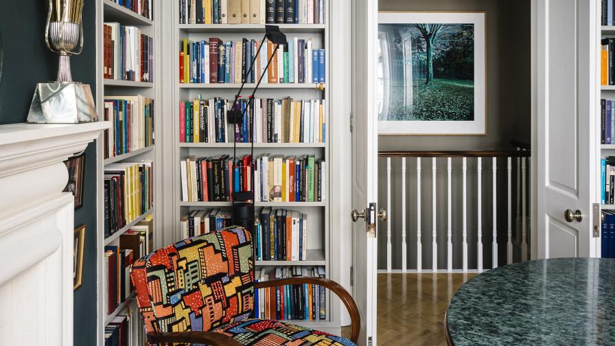 A pair of mid-century modern armchairs are surrounded by bespoke library joinery and earthy green shades