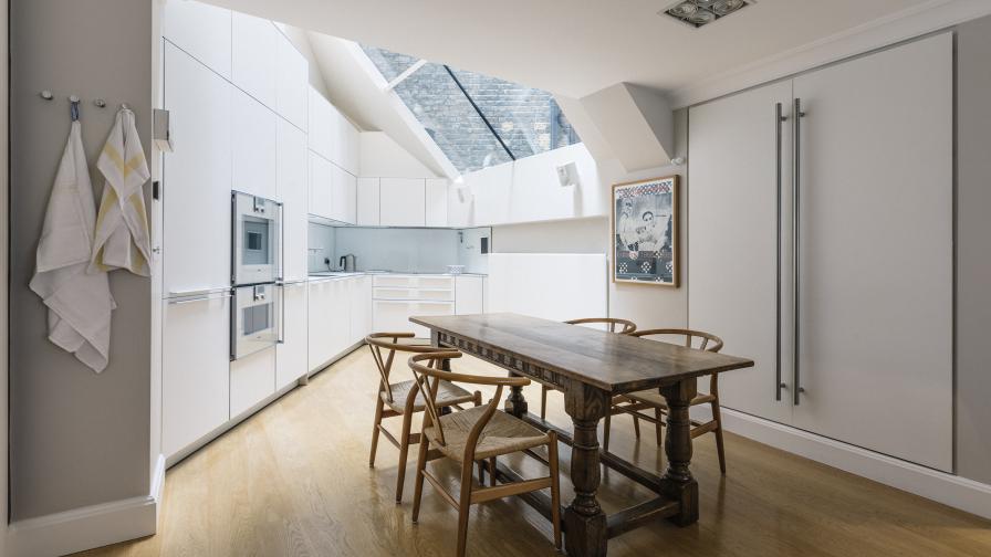 Opening up the roof allows light to poor into the basement kitchen. Strict and clean kitchen units are anchored by the classic rectory table and Mid-Century Modern chairs