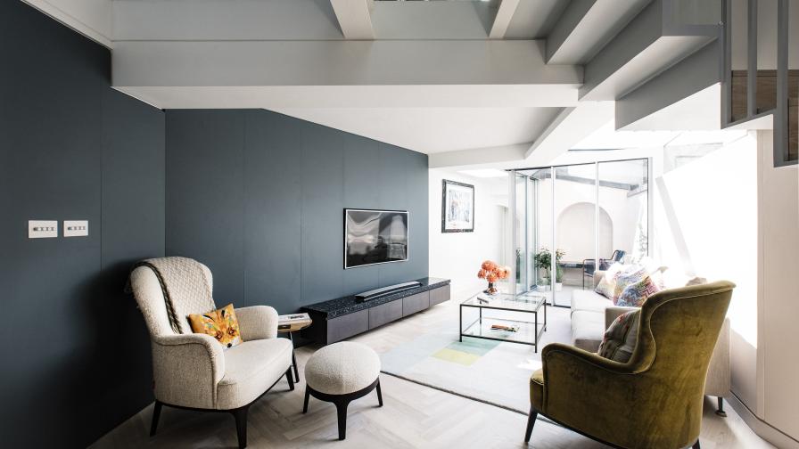 The curving petrol blue wall leads past modern armchairs from the TV room to the walled garden