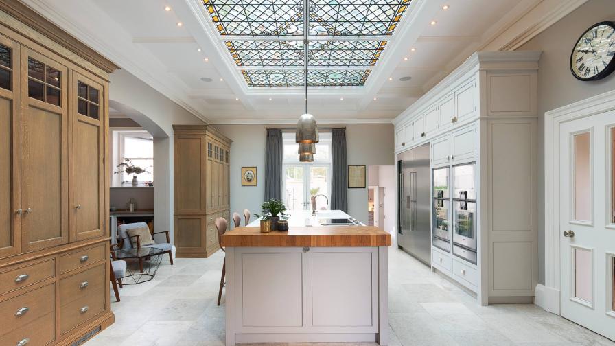 A bespoke kitchen by Hetherington Newman with a white painted island and tall dresser cabinets in oak