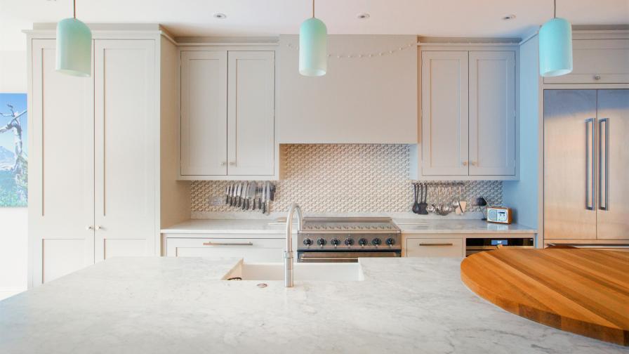 Stepped surfaces of oak and elegant Carrara marble blend seamlessly with the bespoke kitchen, glazed tiles and glass pendant lights