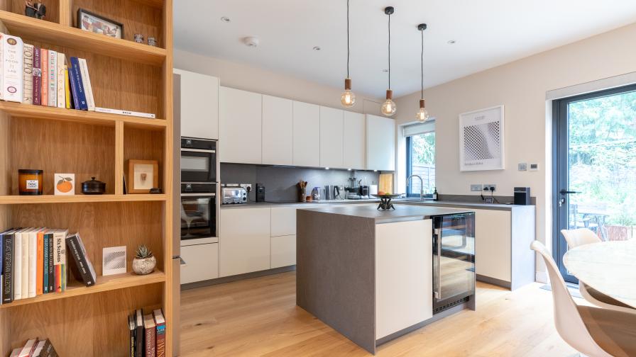 White kitchen featuring grey waterfall island worktop and upstand, Tala pendant lights, and bespoke veneer shelving to define the space