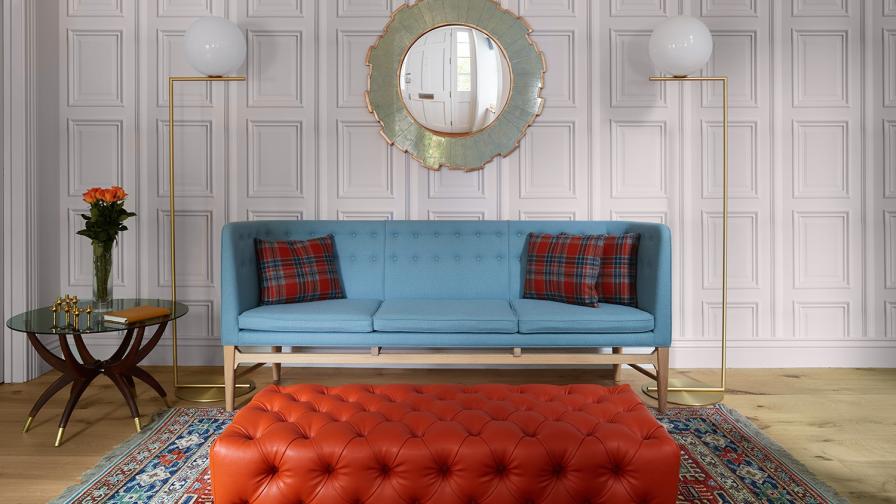 Entrance hall, with blue sofa & feature orange deep buttoned footstool; feature panelling wall paper and design classic lighting.