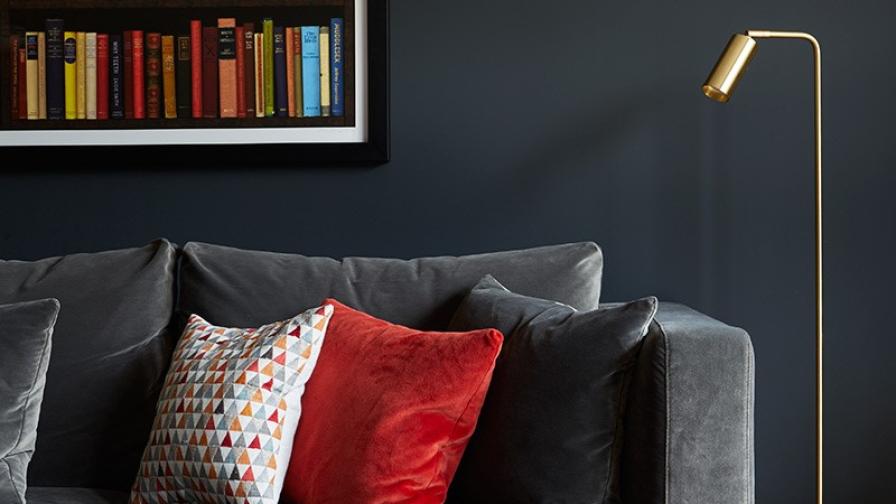 Black walls create a rich family living room, with deep dark grey velvet sofa, accented with orange velvet cushions & brass details.