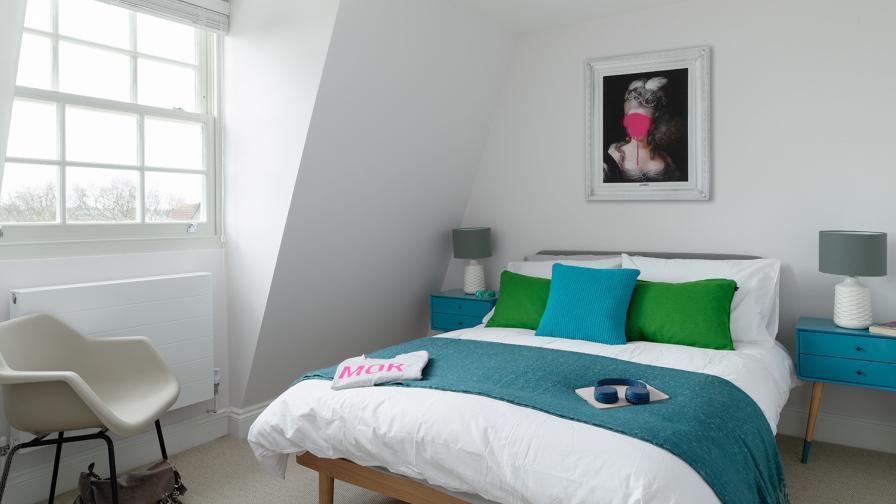 Calm bedroom featuring design classic furniture against a light bright base palette with accent colour pops and bold art work to inject some humour