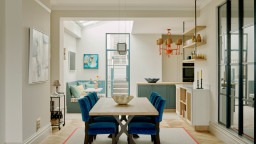 Dining room opened up to kitchen in Victorian townhouse. Crittall screen allows light in.  Neutral room with parquet flooring and dark blue accents