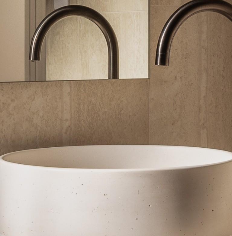Circular sink with curved tap near a mirror.