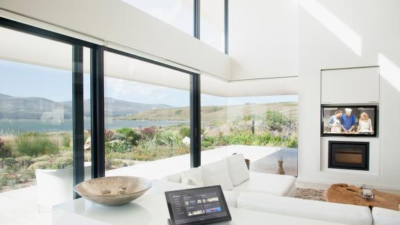 A smart control system atop a counter in a white room with large windows out to a sea view