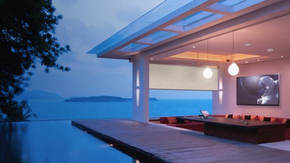 Exterior shot of a home from the garden showing a pool and deck leading on to a living room with a wide screen TV